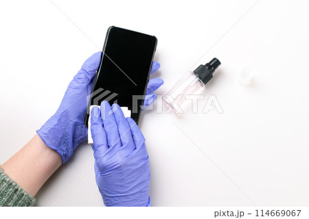 Hands in rubber gloves wipe the phone with disinfectant on a white background. Copy space. Hygiene for the prevention of coronavirus. Health care concept. 114669067