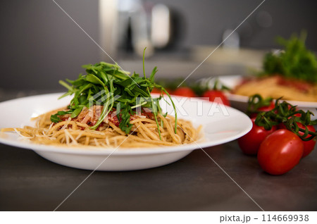 Food background with classic Italian cuisine dish. Pasta spaghetti with tomatoes, arugula leaves and parmesan cheese. Copy advertising space. Classic Italian cuisine dish. Food background with classic Italian cuisine dish. Pasta spaghetti with tomatoes, arugula leaves and parmesan cheese. Copy advertising space. Classic Italian cuisine dish. 114669938
