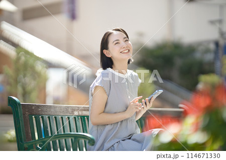 街中のベンチに座ってスマホを見る若い女性 114671330