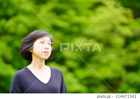 緑の中で黒い服を着て寂し気に立つ中年女性 緑の中で黒い服を着て寂し気に立つ中年女性 114671341