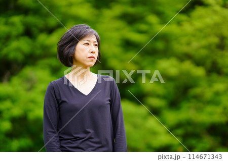 緑の中で黒い服を着て寂し気に立つ中年女性 114671343