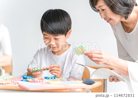 学校の教室でアルファベットのおもちゃを使って英語を勉強する小学生低学年の男の子と女性教師 114672831