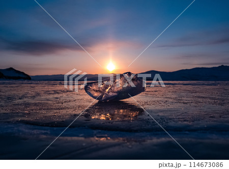 Ice crystal on the frozen surface of Lake Baikal in early morning. Sky and sun reflections on the ice surface. Amazing winter landscape. Winter tourist season at lake Baikal 114673086