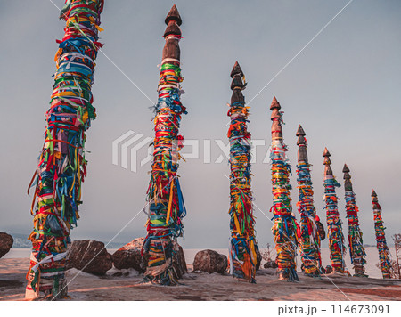 Traditional buryat shaman sacred pillars with colorful ribbons in winter at sunset, cape Burkhan, Olkhon island. Winter Baikal. 114673091