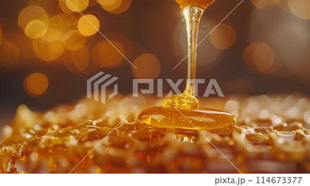 Honey dripping from the wooden honey dropper over thick golden honeycomb on a blurred background. A close up view of the natural organic sweet product. 114673377