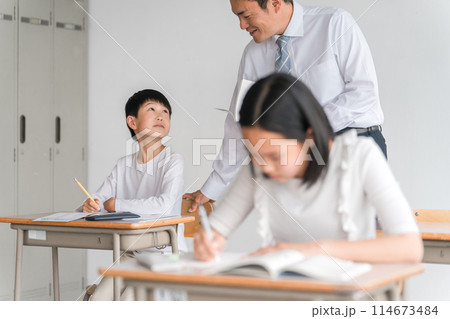 学校の教室・塾で男子生徒に勉強を教える男性教師・塾講師・先生(小学校・学童・学童保育・教育) 学校の教室・塾で男子生徒に勉強を教える男性教師・塾講師・先生(小学校・学童・学童保育・教育) 114673484