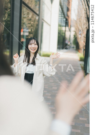 待ち合わせ場所で待ち合わせ相手に手を振る女性 待ち合わせ場所で待ち合わせ相手に手を振る女性 114675412