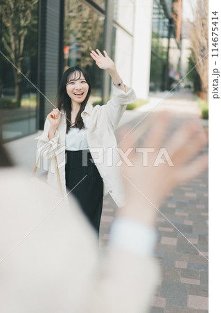待ち合わせ場所で待ち合わせ相手に手を振る女性 114675414