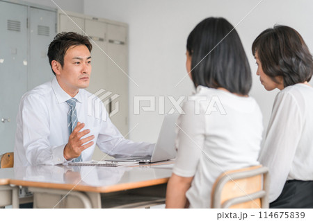 三者面談で厳しい話をする男性担任教師・先生と落ち込む生徒と保護者 114675839