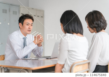 三者面談で厳しい話をする男性担任教師・先生と落ち込む生徒と保護者 114675840