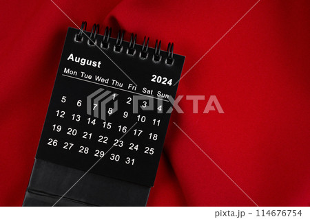 August 2024 Black spiral desktop calendar on red fabric. 114676754