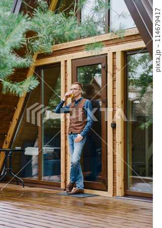 a man goes out onto the wet terrace with a glass of whiskey and enjoys the fresh air after the rain 114679417