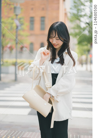 バッグの中がゴチャゴチャで探し物が見つからないからガサゴソしている街を歩く若い女性 バッグの中がゴチャゴチャで探し物が見つからないからガサゴソしている街を歩く若い女性 114680500