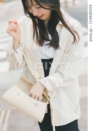 バッグの中からスマホを取り出す街を歩く若い女性 114680504