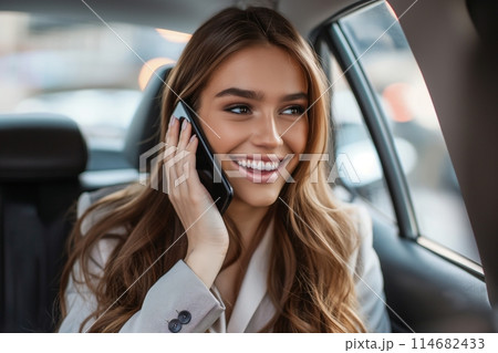 Joyful young woman talking on the phone in a car, showcasing a beaming smile 114682433