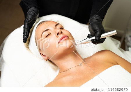 Microneedle RF lifting procedure. A cosmetologist performs a facial rejuvenation procedure on a woman. Hardware cosmetology. 114682970