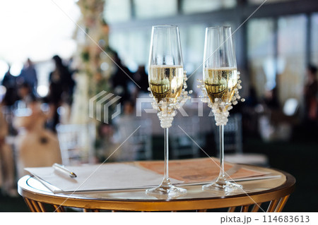 Two wedding glasses stand on a stand against the backdrop of the ceremony arch. Two wedding glasses stand on a stand against the backdrop of the ceremony arch. 114683613