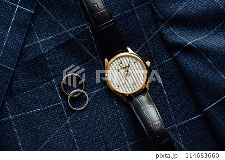Groom's wedding details. Watch, rings and belt placed on a checkered jacket 114683660