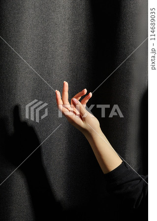 Elegant female hand poised against dark fabric with shadow 114689035
