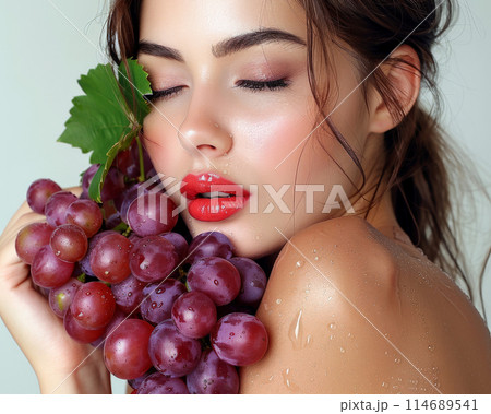 Woman with red lips holding bunch of grapes close to her face, water drops on grapes add freshness 114689541