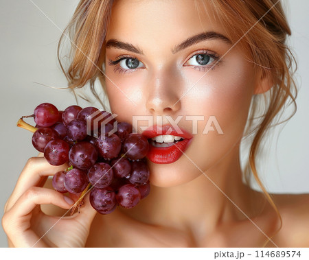 Woman with red lips holding bunch of grapes close to her face, water drops on grapes add freshness Woman with red lips holding bunch of grapes close to her face, water drops on grapes add freshness 114689574