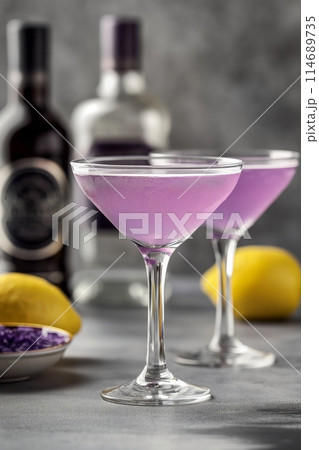 Two Aviation cocktails in focus with bottles and lemon in the background on a textured surface 114689735