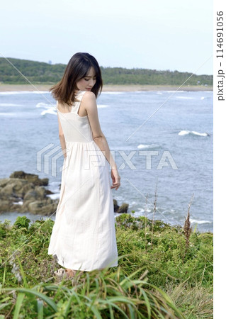 海岸でポーズをとる白いワンピース姿の若い女性 114691056