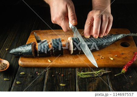 The chef cuts mackerel fish into pieces to prepare a dish for dinner. Low key concept of fish diet. Advertising space The chef cuts mackerel fish into pieces to prepare a dish for dinner. Low key concept of fish diet. Advertising space 114697557