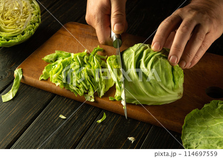 Shredding cabbage with a knife in the hands of a man. The process of preparing sauerkraut on the kitchen table 114697559