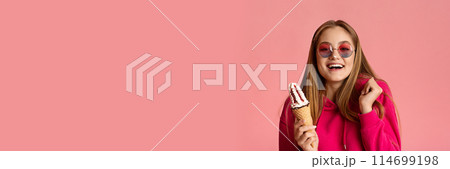 Smiling teenage girl in round glasses with ice cream in her hands gesturing and grimacing on pink studio background, panorama with copy space Smiling teenage girl in round glasses with ice cream in her hands gesturing and grimacing on pink studio background, panorama with copy space 114699198