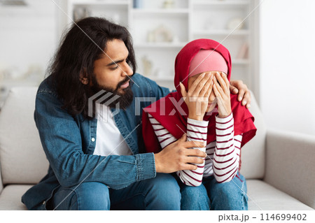 Indian man with long hair is gently comforting a young woman in a red hijab who appears to be upset, her hands covering her face Indian man with long hair is gently comforting a young woman in a red hijab who appears to be upset, her hands covering her face 114699402