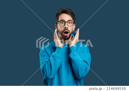 A man wearing glasses with a surprised expression on his face. His eyes widen, eyebrows raise, and mouth forms an O shape in astonishment. The man appears shocked or startled by something unexpected. 114699530