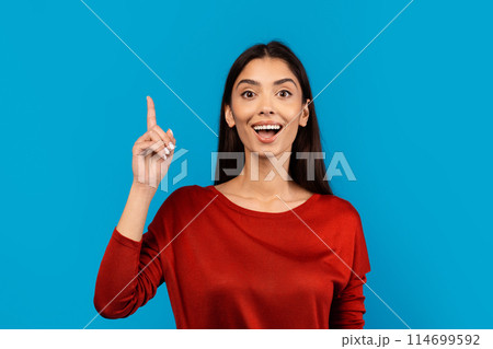 A woman wearing a red shirt is pointing finger up, directing attention to something off-camera. She appears confident and assertive in her gesture, have idea 114699592