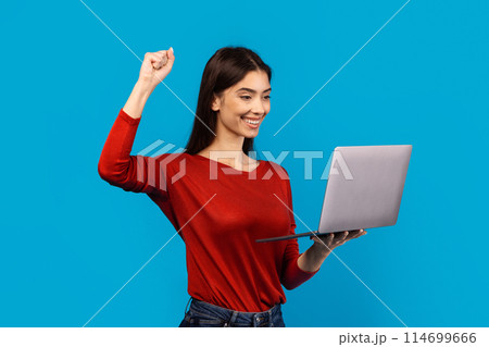 A woman wearing a red shirt is securely holding a laptop computer. Her fingers are visible on the keyboard, indicating she is using it, raising hand up, celebrating success A woman wearing a red shirt is securely holding a laptop computer. Her fingers are visible on the keyboard, indicating she is using it, raising hand up, celebrating success 114699666