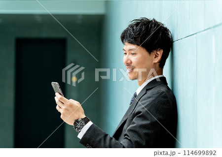 スマホの画面を見る笑顔の男性ビジネスマン 114699892
