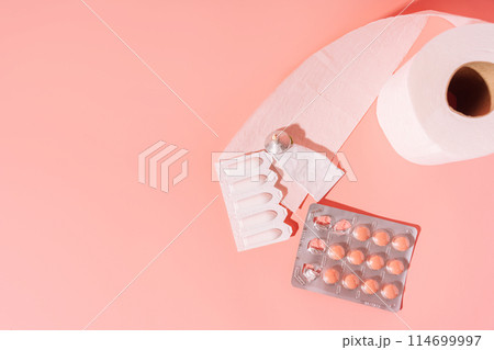 Round tablets and rectal candles in packaging and toilet paper on a pink background 114699997