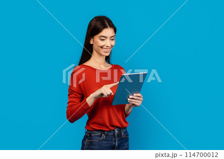 A woman wearing a red shirt is holding a tablet in her hands. She is looking at the screen intently, seemingly engaged with the device. A woman wearing a red shirt is holding a tablet in her hands. She is looking at the screen intently, seemingly engaged with the device. 114700012