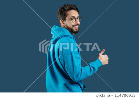 A man wearing a blue hoodie is shown in the image, raising his hand to give a thumbs up gesture. The mans face is not visible, and he appears to be standing against a plain background. 114700015