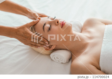 A serene spa setting where a young blonde woman receives a gentle facial massage, promoting a sense of relaxation and wellbeing 114700024
