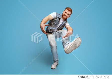 Come on. Smiling millennial caucasian guy, fool around and marked out with hands at camera, full length, blue studio background. 114700388