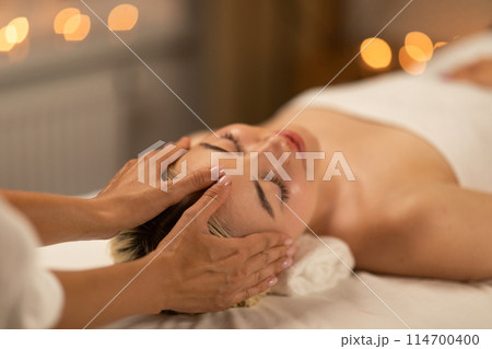 A calming scene at a spa with a young blonde woman receiving a delicate facial massage, showcasing her relaxed demeanor and comfort. A calming scene at a spa with a young blonde woman receiving a delicate facial massage, showcasing her relaxed demeanor and comfort. 114700400
