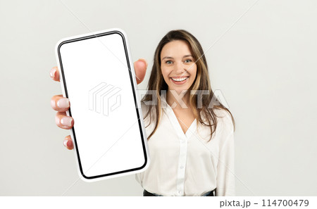 A woman entrepreneur holding a cell phone up in front of her with a blank screen visible. She appears to be examining the phone closely, possibly checking for notifications or composing a message. 114700479