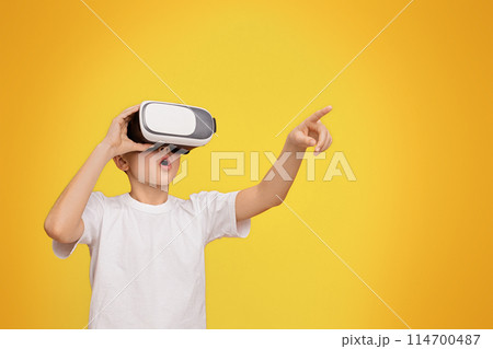 Wow, its amazing. Boy experiencing virtual reality, gesturing on orange studio background, copy space 114700487