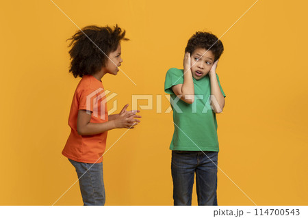 African American young girl appears to be talking animatedly to a boy, who is covering his ears with his hands, possibly indicating he is not interested in hearing what she has to say. 114700543