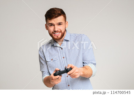 Gambling addiction. Young guy holding joystick and playing video games on studio background, panorama, copy space 114700545