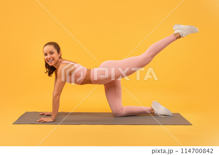 A woman dressed in pink clothing is actively engaging in a yoga pose, showcasing flexibility and strength. She holds the pose with poise and focus, demonstrating balance and concentration. 114700842