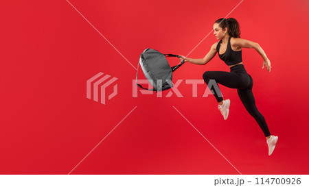 An athletic woman dressed in a black tank top and leggings is captured mid-run as she reaches out to grab a grey backpack, copy space An athletic woman dressed in a black tank top and leggings is captured mid-run as she reaches out to grab a grey backpack, copy space 114700926