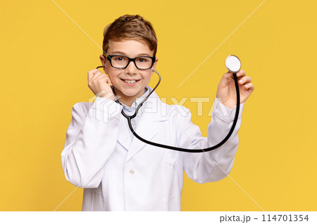 Smiling little boy in medical uniform playing with stethoscope, orange panorama background with free space 114701354