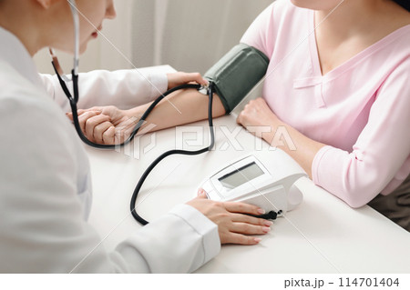 A doctor is using a stethoscope to measure a patients blood pressure in a medical setting. The doctor is focused on listening to the patients heartbeat and recording the readings on a medical chart. A doctor is using a stethoscope to measure a patients blood pressure in a medical setting. The doctor is focused on listening to the patients heartbeat and recording the readings on a medical chart. 114701404