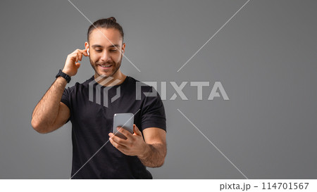 A man wearing a black shirt is standing while holding a smart phone in his hand, focusing on the screen with a serious expression, copy space 114701567